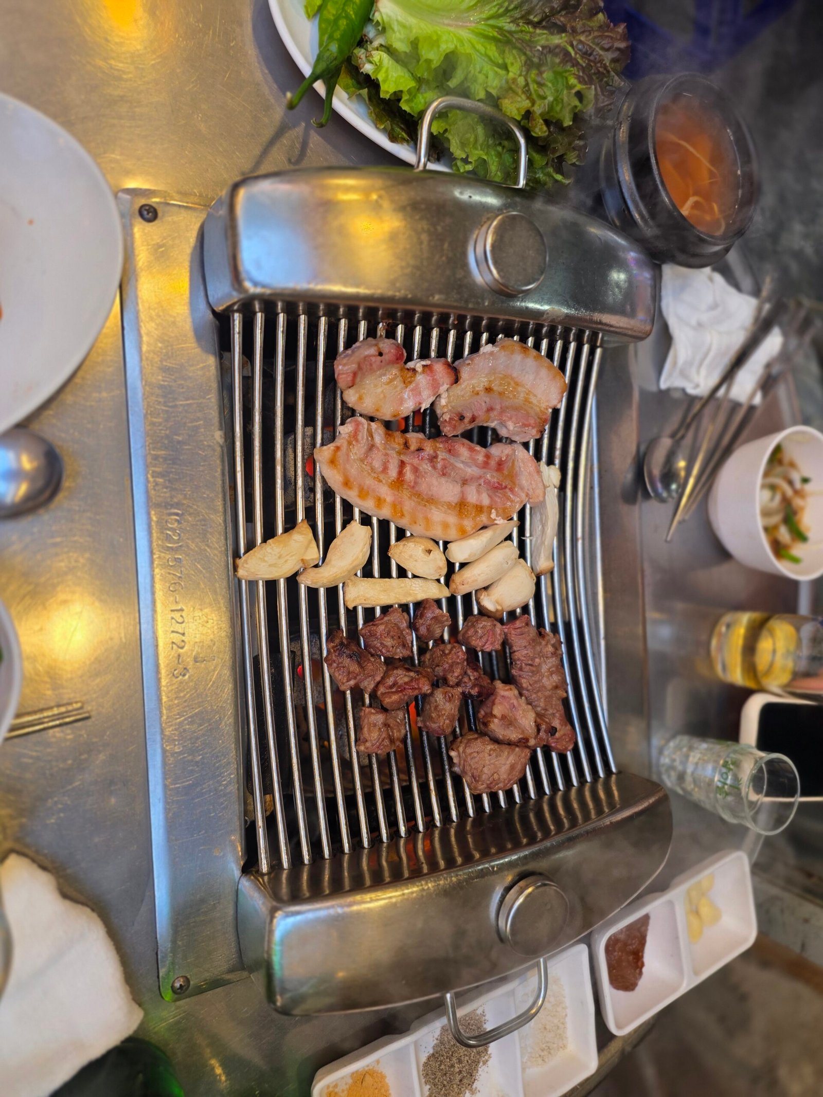Pork belly, beef pieces and mushrooms on a Korean barbecue grill.
