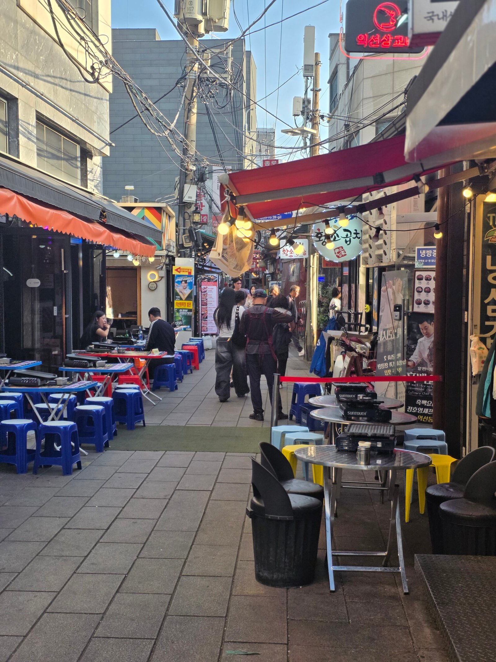 Outdoor restaurant tables and stools lining a narrow Jongno 3-ga street.