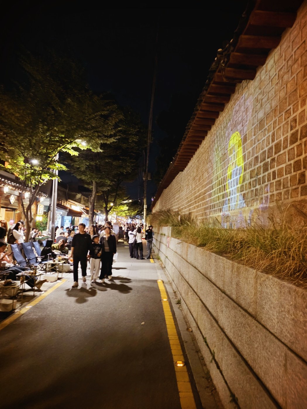 Seosulla-gil at night, with outdoor dining and the illuminated Jongmyo stone wall