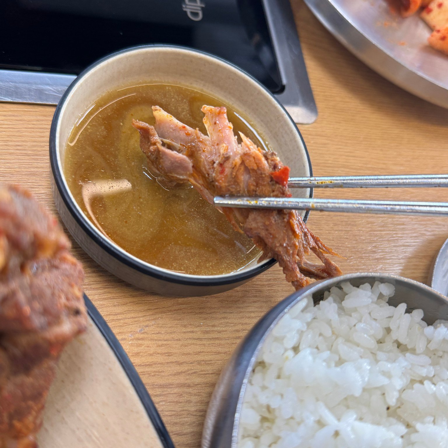 Chopsticks lifting separated pork above a small dipping-sauce dish beside rice