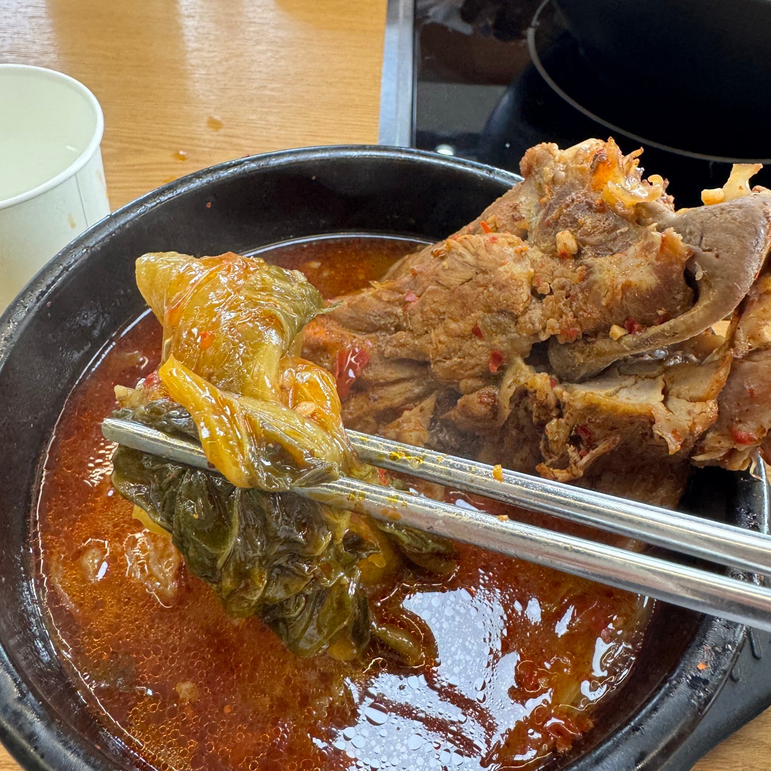 Metal chopsticks holding leafy greens above red pork backbone soup
